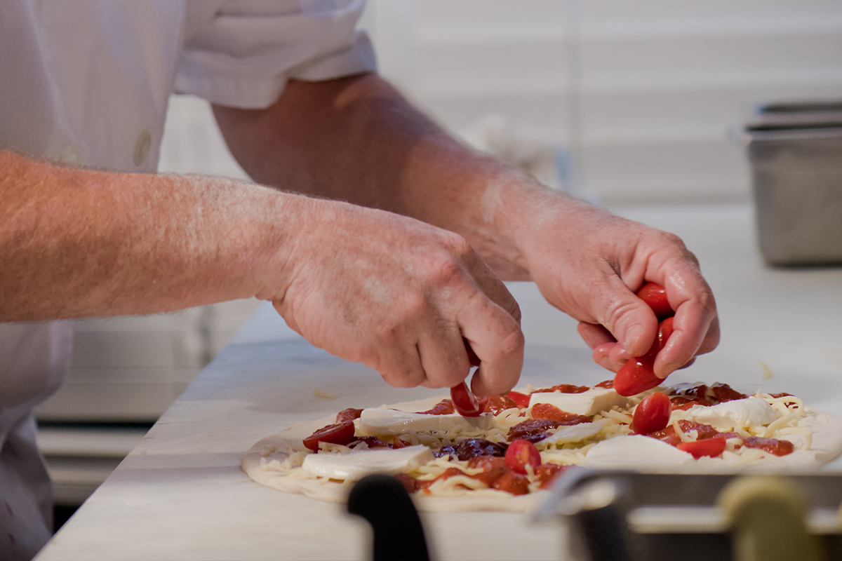 upclose of chef hands prepping a pizza with tomatoes